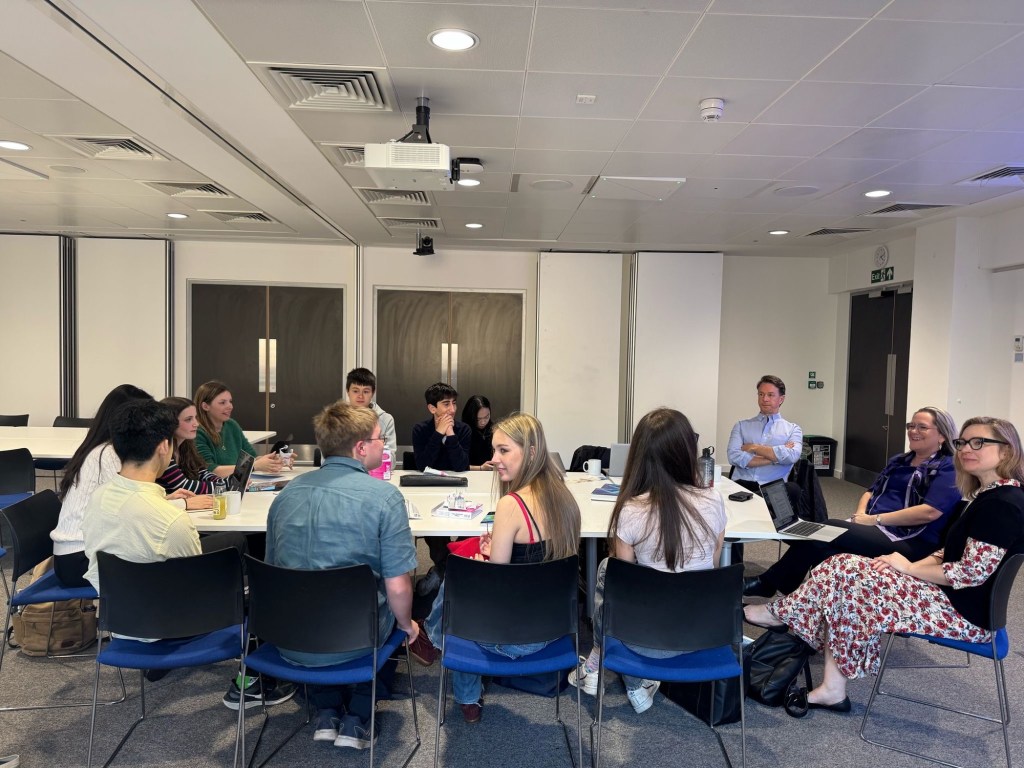 Interns and mentors seated around a large table in a seminar room, in discussion