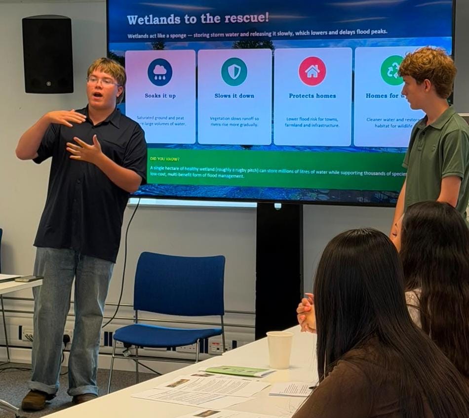 A young person explaining a slide headed Wetlands to the rescue, showing how wetlands soak up and slow floodwater, protect homes and provide habitat