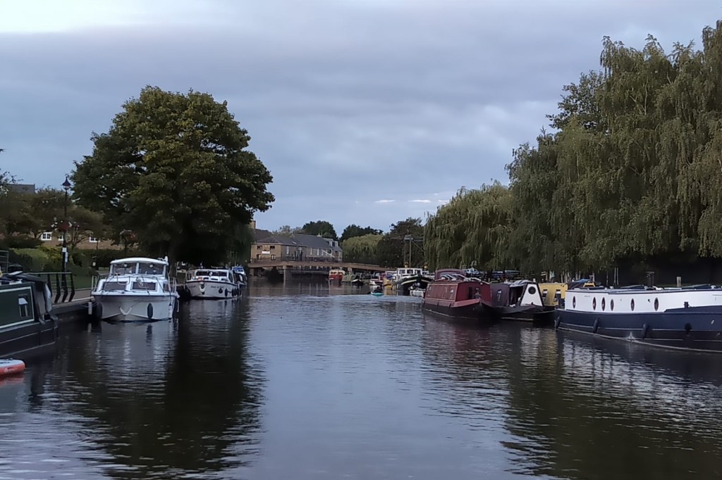A river running past moored narrowboats and houses at the edge of a town