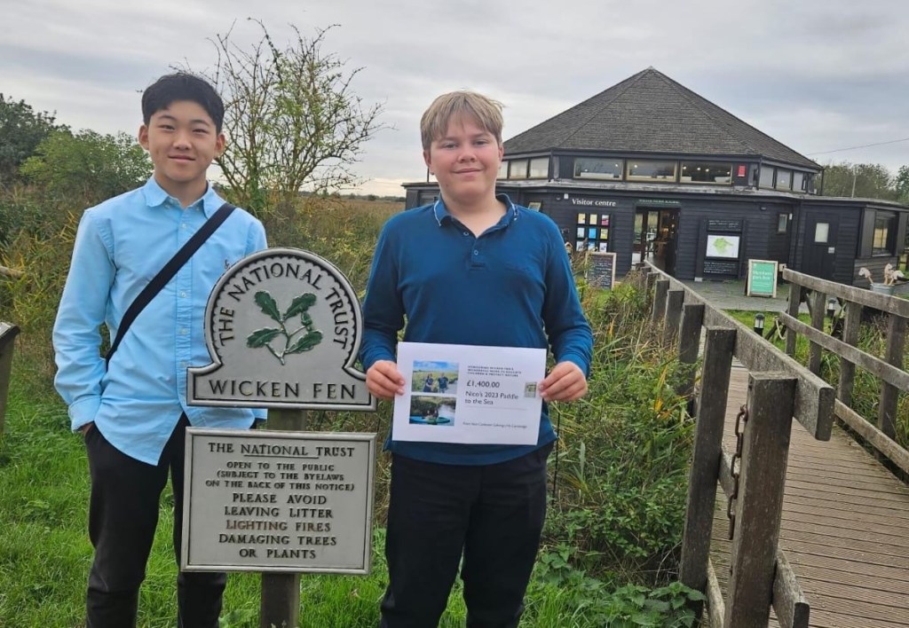 Two young people standing beside a nature reserve sign, holding a printed booklet
