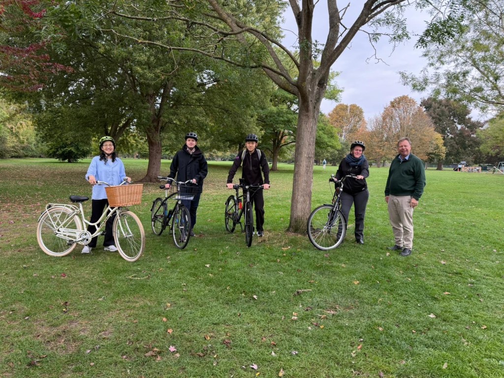 A group of young people standing with bicycles on grass beneath trees